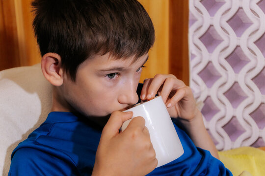 A close-up shows a boy relaxing indoors, drinking from a white mug with a spoon inside an image that evokes associations with warm tea, hydration, coziness, recovery from illness, and home care.
