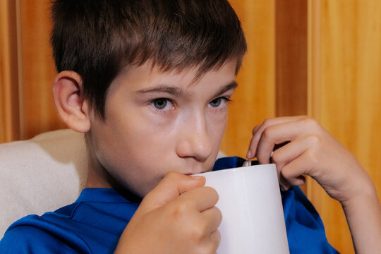 A close-up shows a boy relaxing indoors, drinking from a white mug with a spoon inside an image that evokes associations with warm tea, hydration, coziness, recovery from illness, and home care.