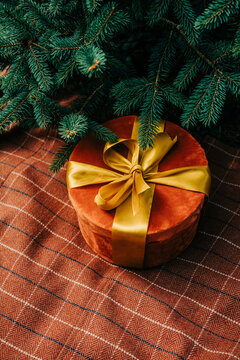 Christmas gift box with bow beside fir branch on brown checkered tablecloth, side view