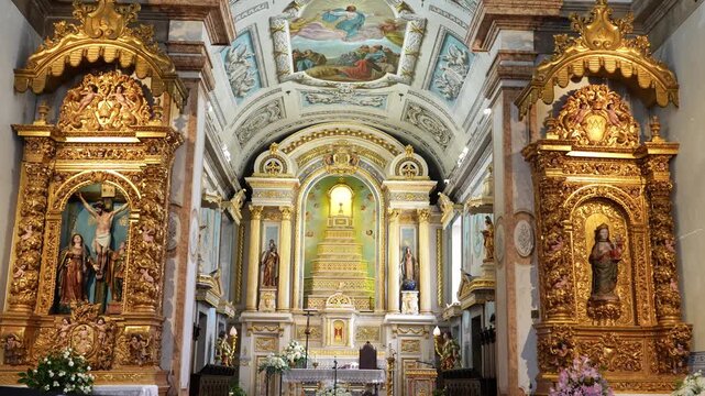 Interior view of a historic catholic church, featuring a richly decorated golden baroque altar and religious statues