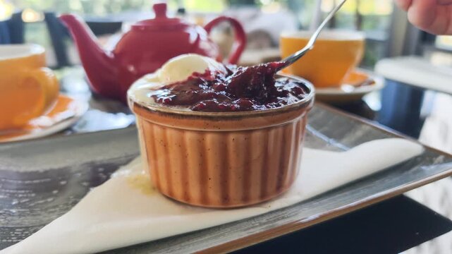 Spoon scoops chocolate fondant during sweet tasting process in cozy cafe. Teatime tasting process shows hot lava cake topped with berry jam and vanilla ice cream served in ceramic ramekin close up.