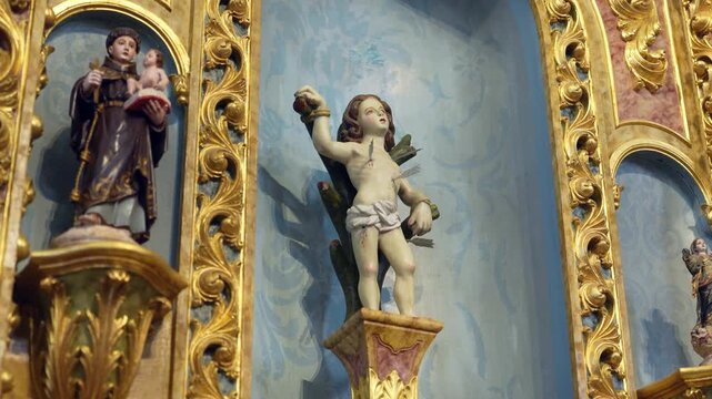 Ornate golden altarpiece detailing religious statues including a young Saint Sebastian bound with arrows and Saint Anthony holding baby Jesus