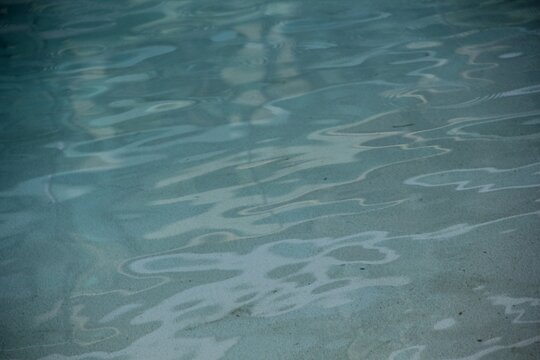 Abstract view of light blue pool water surface with soft wavy ripples and light reflections over a smooth bottom.