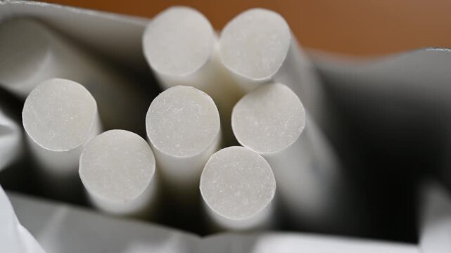 Extreme macro close-up of cigarette filters sliding staggered from pack edge