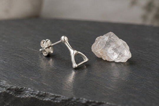 Sterling silver stapes bone earring and quartz crystal on dark slate, jewelry presentation.