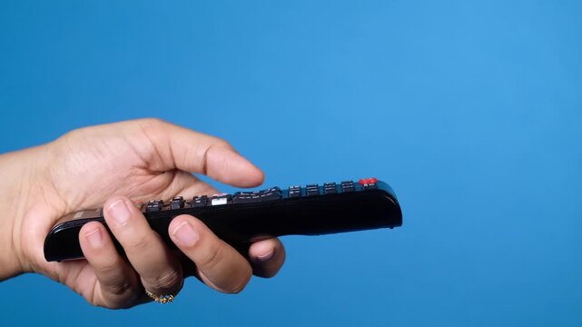 Hand holding remote control and pressing buttons to change channels