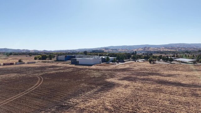 Wide aerial shot revealing the Solano Community College campus buildings and surrounding dry fields in Vacaville, California, with rolling hills visible on the horizon under a clear blue sky