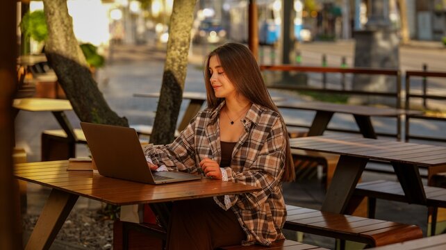 Young woman working on a laptop at an outdoor cafe table during golden hour
