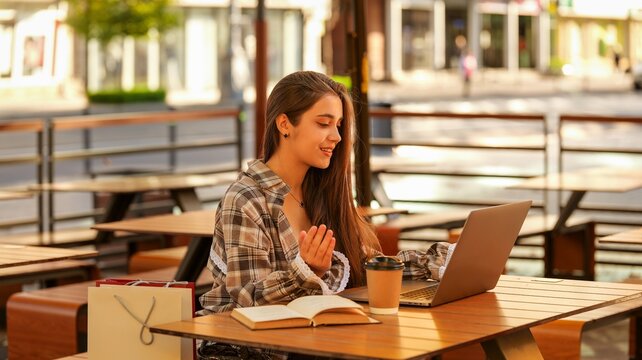 Young woman working on laptop at outdoor cafe table with coffee and shopping bags
