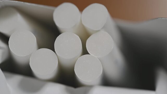 Extreme macro close-up of cigarette filters sliding staggered from pack edge