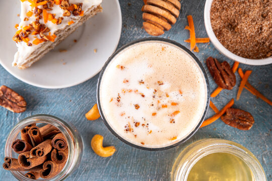 Tasty autumn carrot cake or carrot spice coffee latte, topped with whipped creamy foam, sweet syrup, crushed pecan nuts and sliced carrots, with cinnamon and pumpkin pie spices