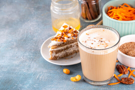 Tasty autumn carrot cake or carrot spice coffee latte, topped with whipped creamy foam, sweet syrup, crushed pecan nuts and sliced carrots, with cinnamon and pumpkin pie spices