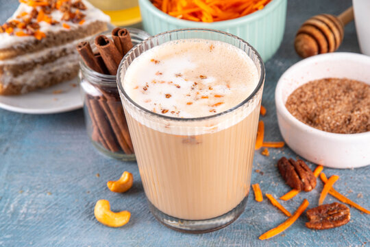 Tasty autumn carrot cake or carrot spice coffee latte, topped with whipped creamy foam, sweet syrup, crushed pecan nuts and sliced carrots, with cinnamon and pumpkin pie spices