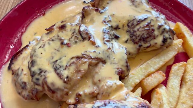 Tracking shot over a peri peri chicken and chips in a plate on a wooden table.