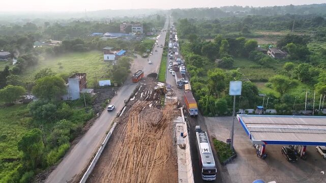 Dynamic high angle aerial following a single lane of stalled traffic forced into a tight detour by an unfinished elevated road expansion in India.