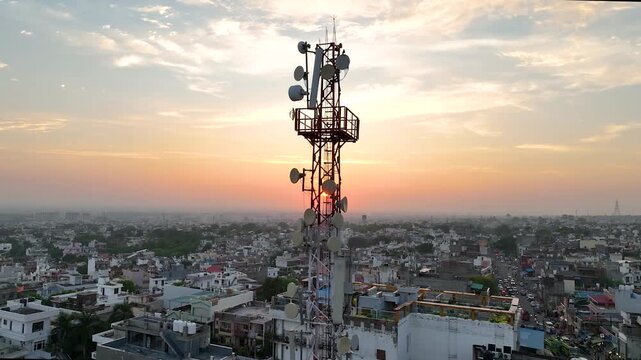 Cinematic drone tracking shot circling a cellular 5G network mast in an overpopulated urban Indian town.