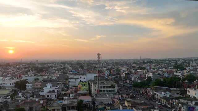 Cinematic aerial push towards cellular base station mast against radiant sunset in overpopulated Indian town.