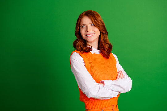 Smiling redhead woman in orange sweater poses confidently against a green studio background, cheerful portrait conveying happiness, friendliness and thoughtful optimism