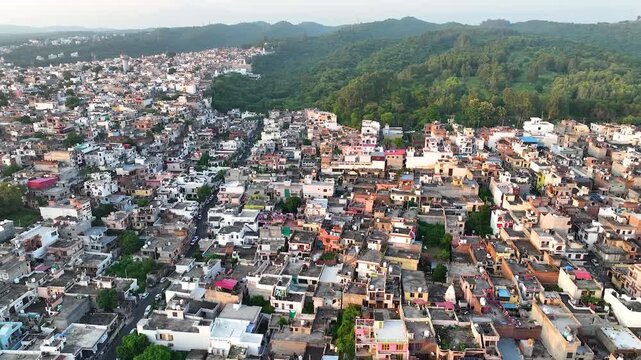 Aerial establishing shot of rapid unplanned city growth and urban sprawl encroaching on green hills in India.