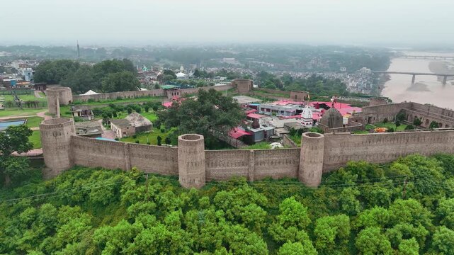 Cinematic 4K drone circling shot of ancient Bahu Fort ramparts and Bave Wali Mata temple on lush green hill.