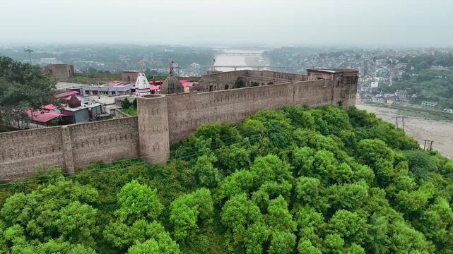 Aerial pullback from Bahu Fort revealing Tawi River, Jammu city skyline, and river bridges in monsoon season.