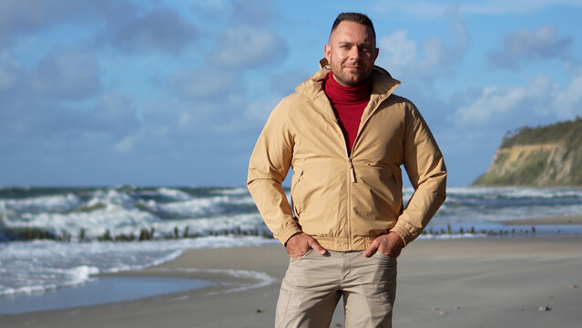 Front view of a confident man standing on the sea coast in autumn with a cliff on the background.