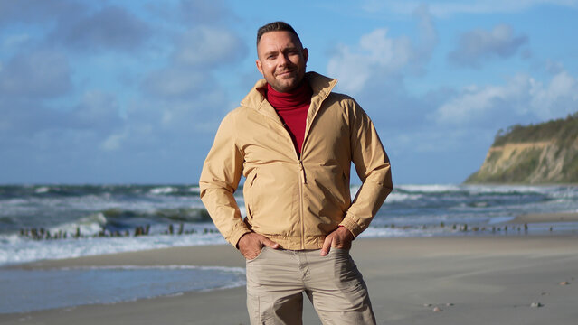 Front view of a confident man standing on the sea coast in autumn with a cliff on the background.