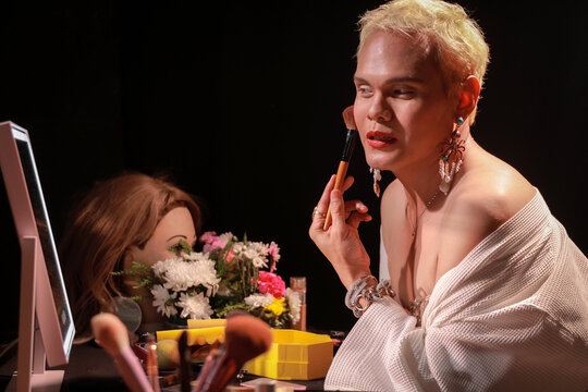 Feminine man  applies cosmetic products carefully, creating an alternative makeup look with intense focus. artist perfects their appearance