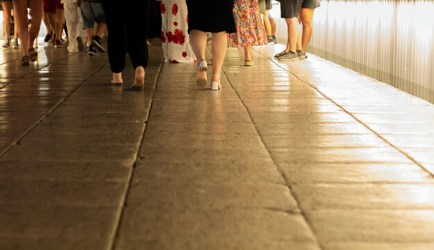 Night crowd. Group of people crosses a pedestrian bridge with an illuminated railing at night. Low-angle shot. Adobe RGB color profile. Real Photo.