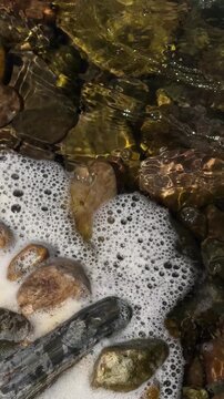 White Foam Swirling Around River Stones in Shallow Water