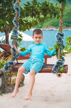 happy boy schoolchild swinging on a swing on the beach by the sea during a summer vacation at tropical resort
