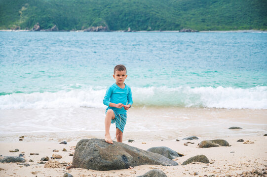 boy schoolchild is posing by the beach by the sea during a summer vacation at tropical resort.