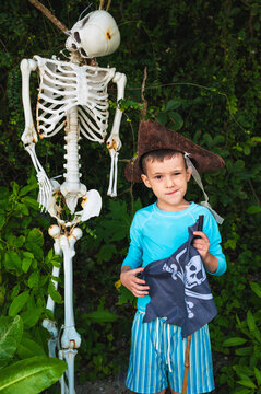 schoolboy child boy in a pirate hat with a flag standing next to a skeleton during summer vacation