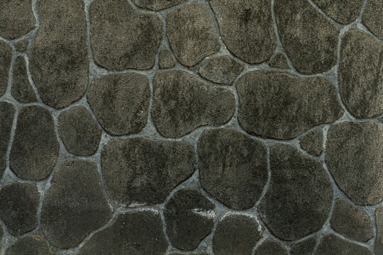 Dark stone wall texture background with irregular natural river rocks. Rustic black cobble stone cladding wall pattern background for architecture design
