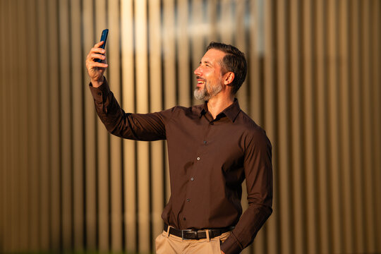 Mature man smiling taking selfie with smartphone outdoors