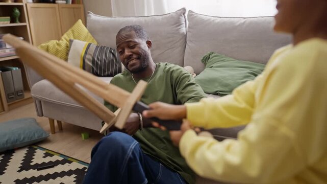 African American father playing toy wooden sword fight with young son at home. Clip conveys positive parenting, ideal for family lifestyle campaigns, fatherhood storytelling, and commercials