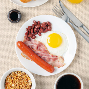 Hearty homemade family breakfast. Eggs, bacon, sausages, beans, croissants, toast and coffee on the table. Top View