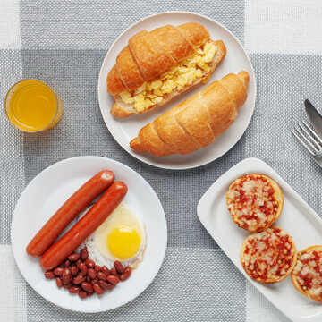 Hearty homemade family breakfast. Eggs, bacon, sausages, beans, croissants, toast and coffee on the table. Top View