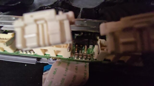 Extreme close-up macro shot of an internal electronic PCB board with disconnected white wire header plugs hovering above sockets, featuring ribbon cable on a dark surface.