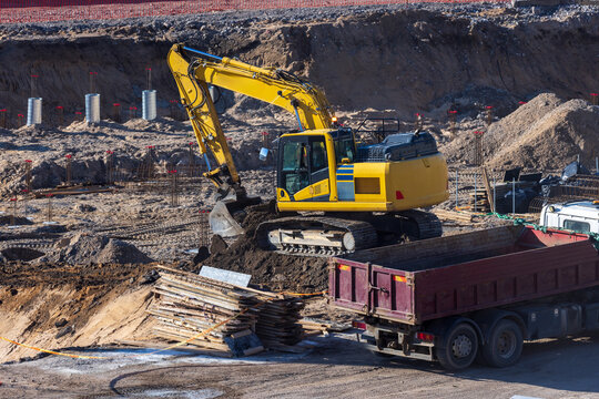 View of a yellow excavator digging at a construction site with a dump truck and foundation work in Vilnius, Vilnius County, Lithuania.