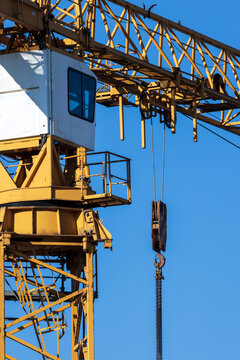 View of a yellow construction crane with a metal lattice structure, operator cabin, and pulley system with a heavy chain against a clear blue sky in Vilnius, Vilnius County, Lithuania.