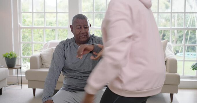 African American woman holding hand rolling sleeve guiding male arm stretch for mobility by window