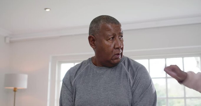 Senior African American dad in grey top lifting hex weights at home after daughter cue spotting