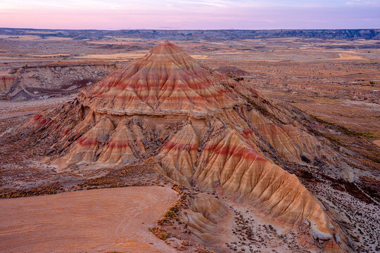View of the unique clay and sandstone rock formations of Bardenas Reales, featuring layered sedimentary hills under a soft sunset sky in Spain.