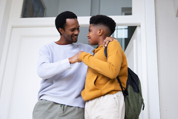 Naklejka premium African American dad and teen son leaning, bumping fists on doorstep with olive backpack
