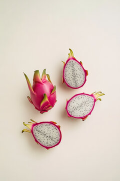 A minimalist photograph featuring a dragon fruit on a white background, with some cut in half in the bottom left corner. The central fruit is in focus, creating a soft, pastel beige tone.