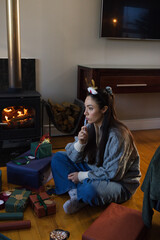 Obraz premium Woman sitting cross-legged on hardwood floor near wood-burning stove in gray sweater planning gifts