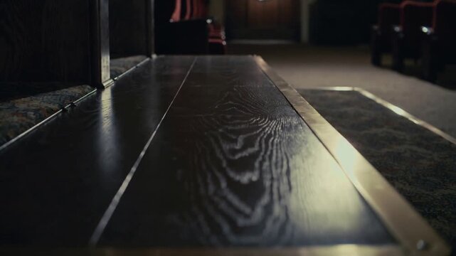 Gliding low-angle camera revealing pew edge at chapel, highlighting wood grain and brass trim