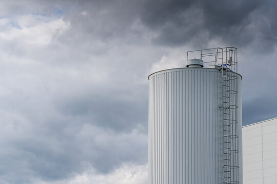 View of a white industrial storage silo with a metal ladder against a cloudy sky in Poland.