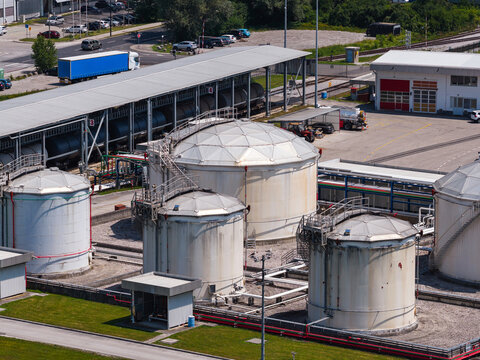 Aerial view shows oil storage tanks and petroleum facility in an industrial area with trucks at the site.